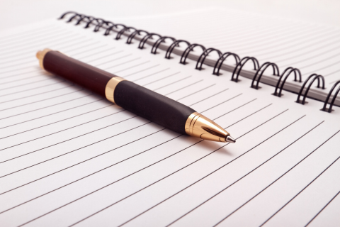 Black and gold pen laying on a lined notepad